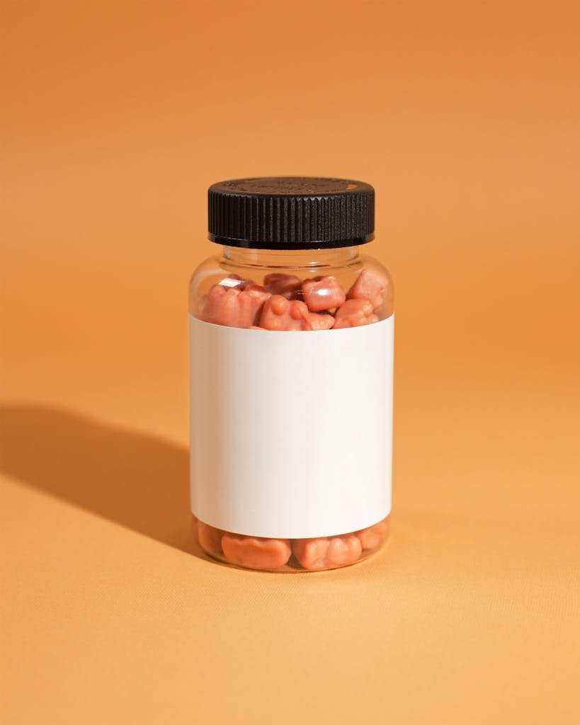 A clear jar with orange gummies against a vibrant orange background, ideal for product showcases.